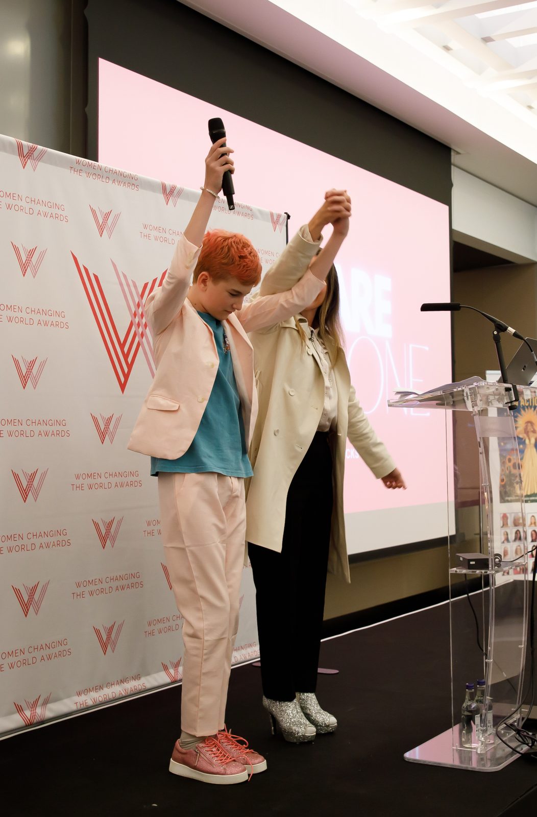 Tanya raising a child’s hand on stage while the child holds a microphone aloft
