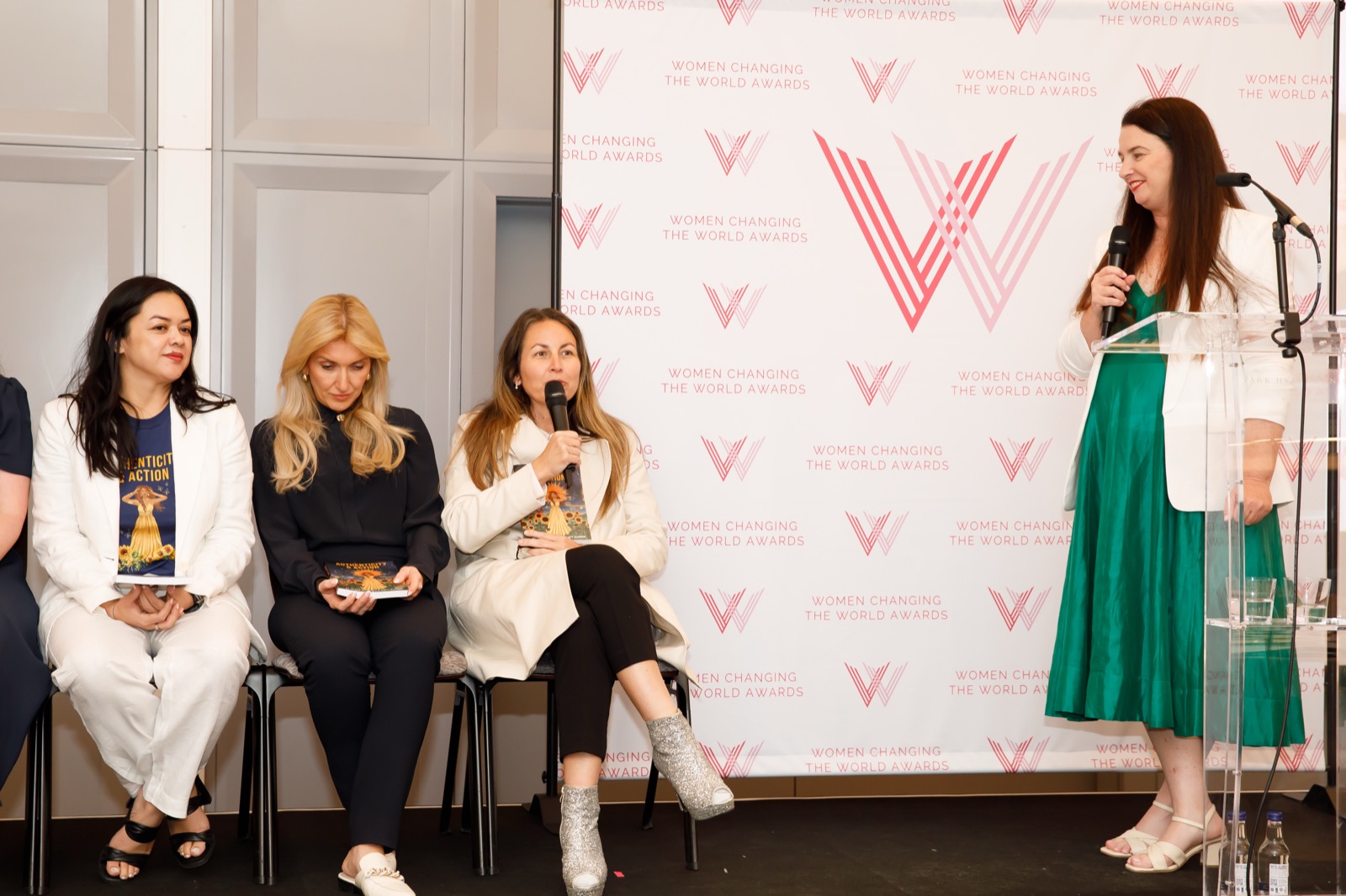 Tanya Hicks speaking into a microphone on a panel in front of a Women Changing the World Awards backdrop